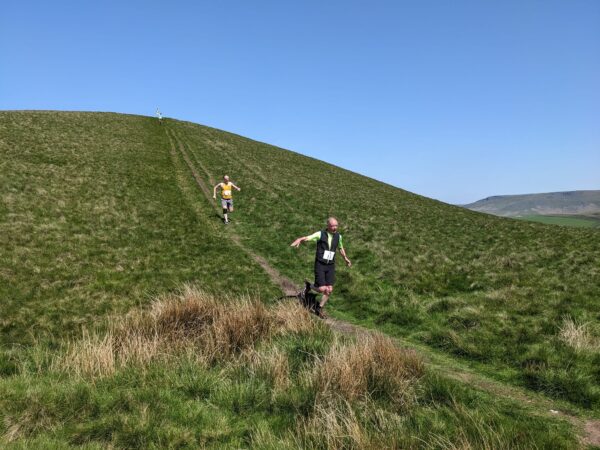 Widely spaced runners running downhill across moorland in bright sunny weather.