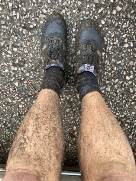 A pair of legs wearing muddy Walsh fell running shoes