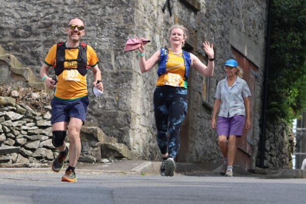 Matt Broadhead and Elin Reeves run down hill towards the camera. Elin is waving.